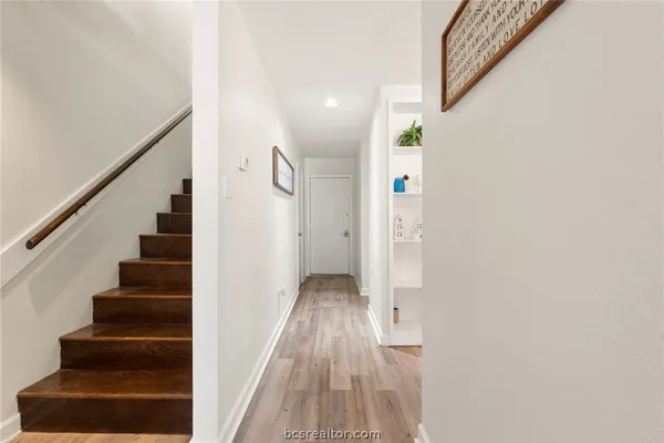 a view of a hallway with wooden floor and a bathroom