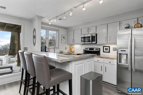 a kitchen with stainless steel appliances granite countertop a dining table chairs refrigerator and sink