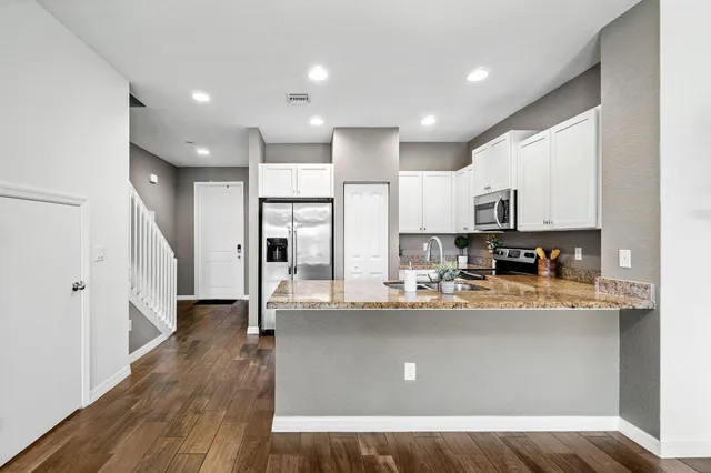 a kitchen with stainless steel appliances granite countertop a refrigerator a sink dishwasher a stove and white cabinets with wooden floor