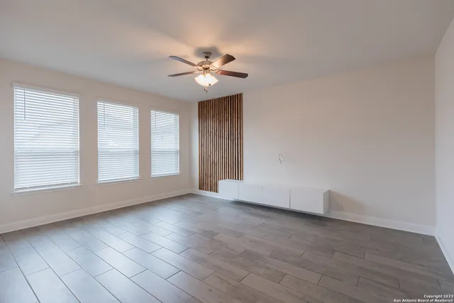 an empty room with wooden floor fan and windows
