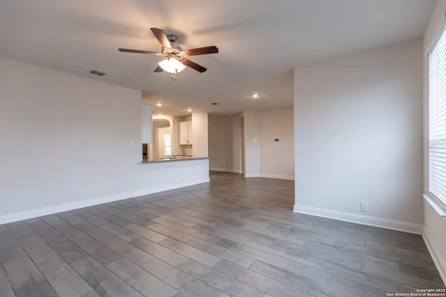 a view of an empty room with wooden floor and a ceiling fan