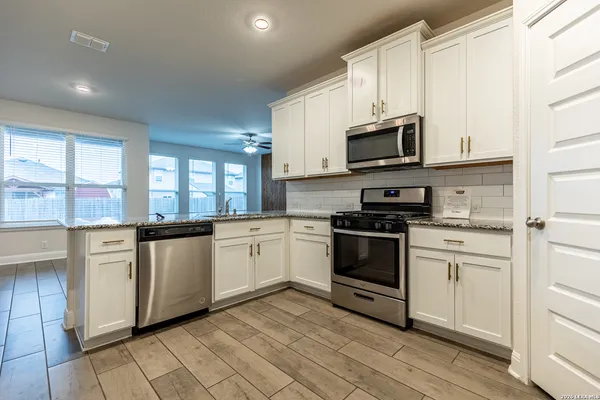 a kitchen with stainless steel appliances granite countertop white cabinets a sink a stove a microwave and a window