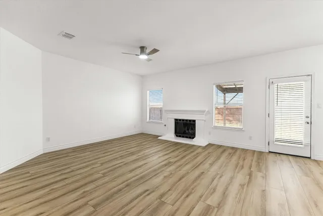 an empty room with wooden floor fireplace and windows