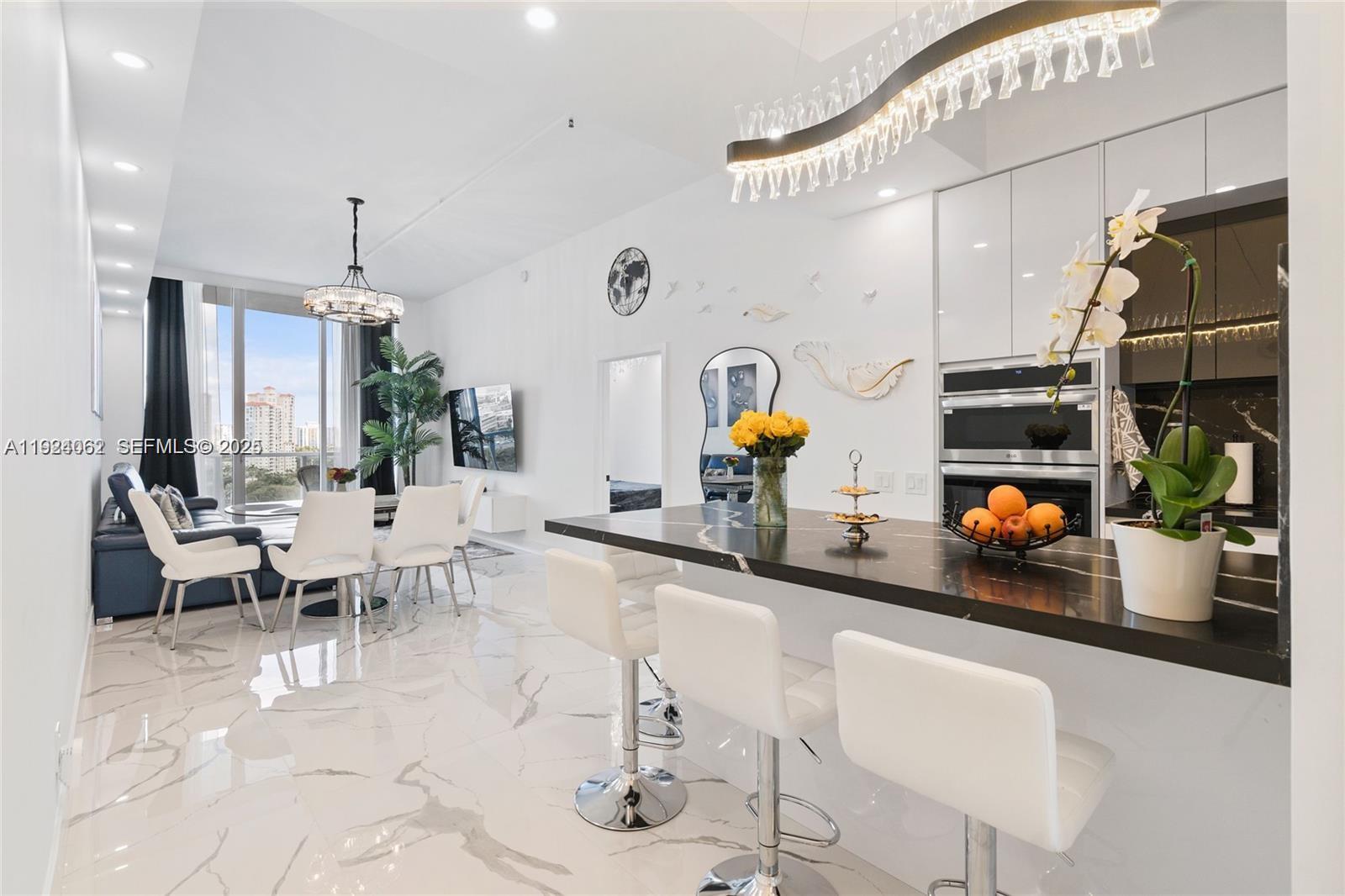 a living room with stainless steel appliances furniture a chandelier and a kitchen view