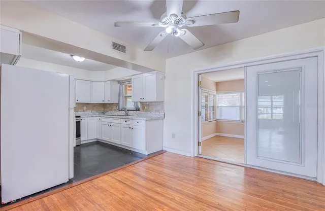 an empty room with wooden floor a ceiling fan and windows