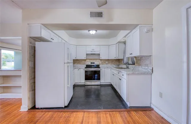 a kitchen with stainless steel appliances granite countertop a refrigerator a sink dishwasher a stove and white countertops with wooden floor