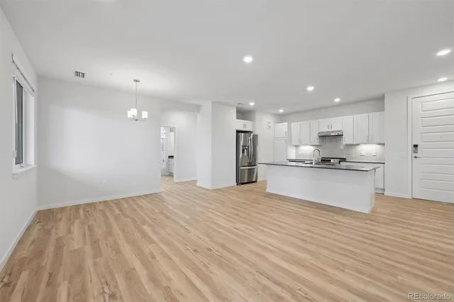 a view of kitchen with kitchen island a sink wooden floor white stainless steel appliances and cabinets