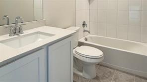 4304 Placer Mine Road Aubrey, TX 76227 - Photo 9 of 12 Bathroom featuring a white vanity with an integrated sink, polished chrome faucet, a standard white toilet, a white bathtub with subway tile surround, and large format floor tiling