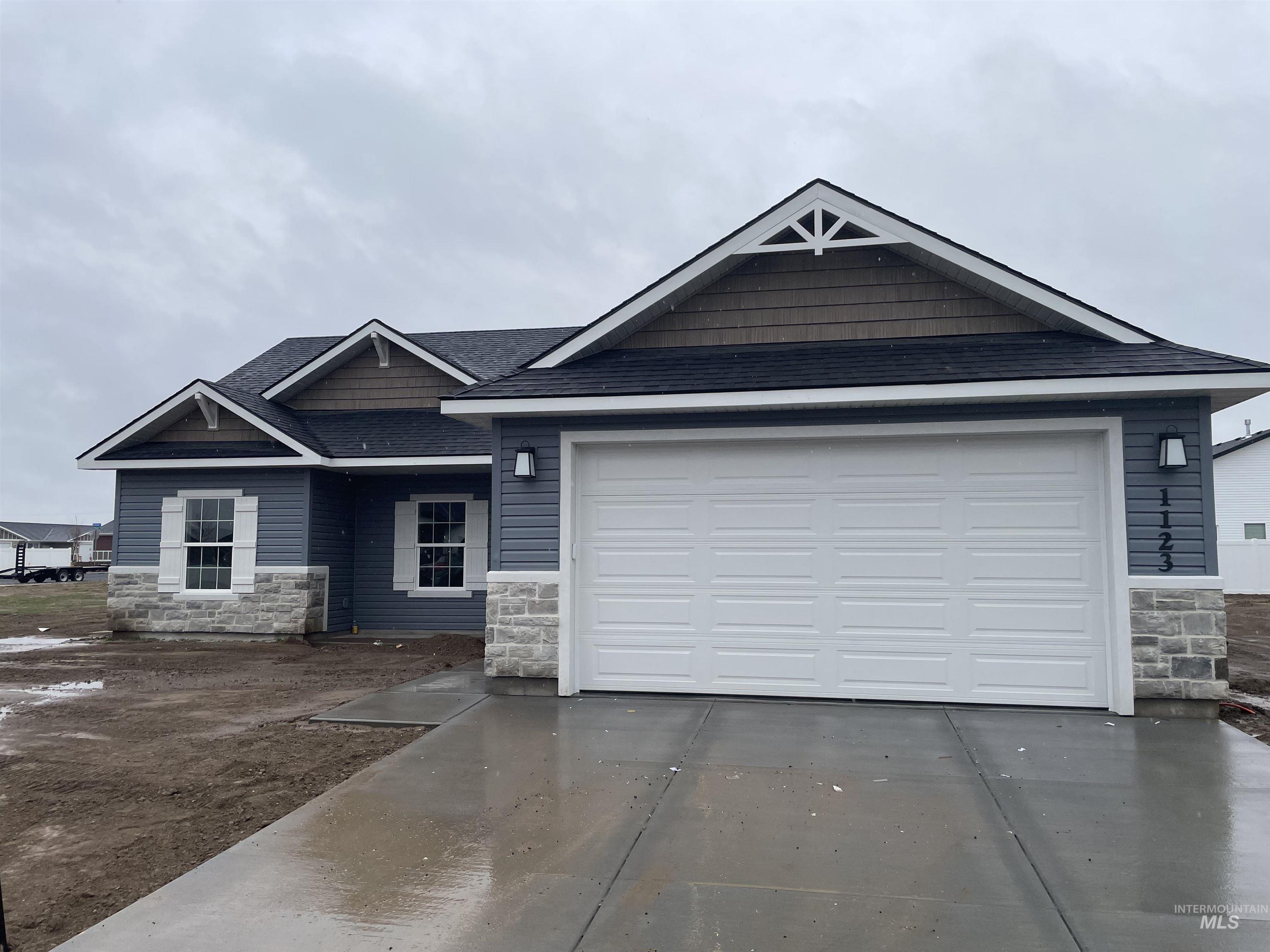 View of front of house with stone siding, a shingled roof, driveway, and a garage