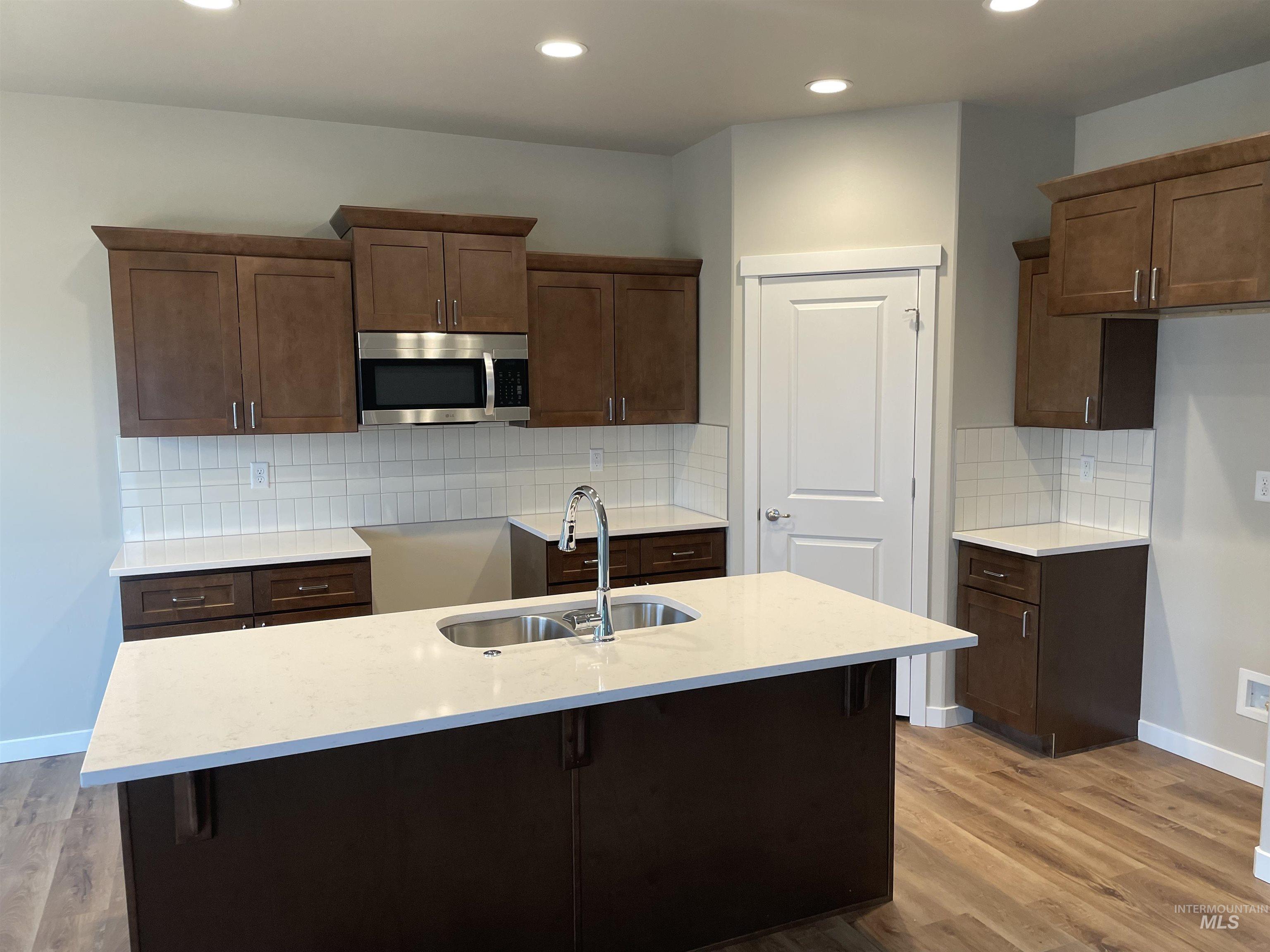 1123 Frank Henry Road Twin Falls, ID 83301 - Photo 2 of 20 Kitchen featuring stainless steel microwave, light wood-type flooring, tasteful backsplash, light stone countertops, and an island with sink