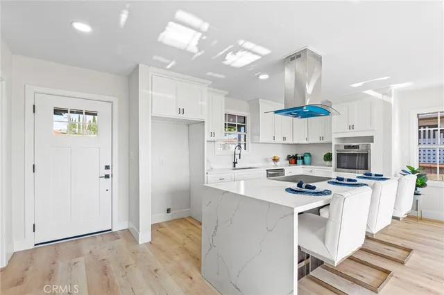 a kitchen with stainless steel appliances a stove a sink dishwasher a refrigerator white cabinets and wooden floor next to a window