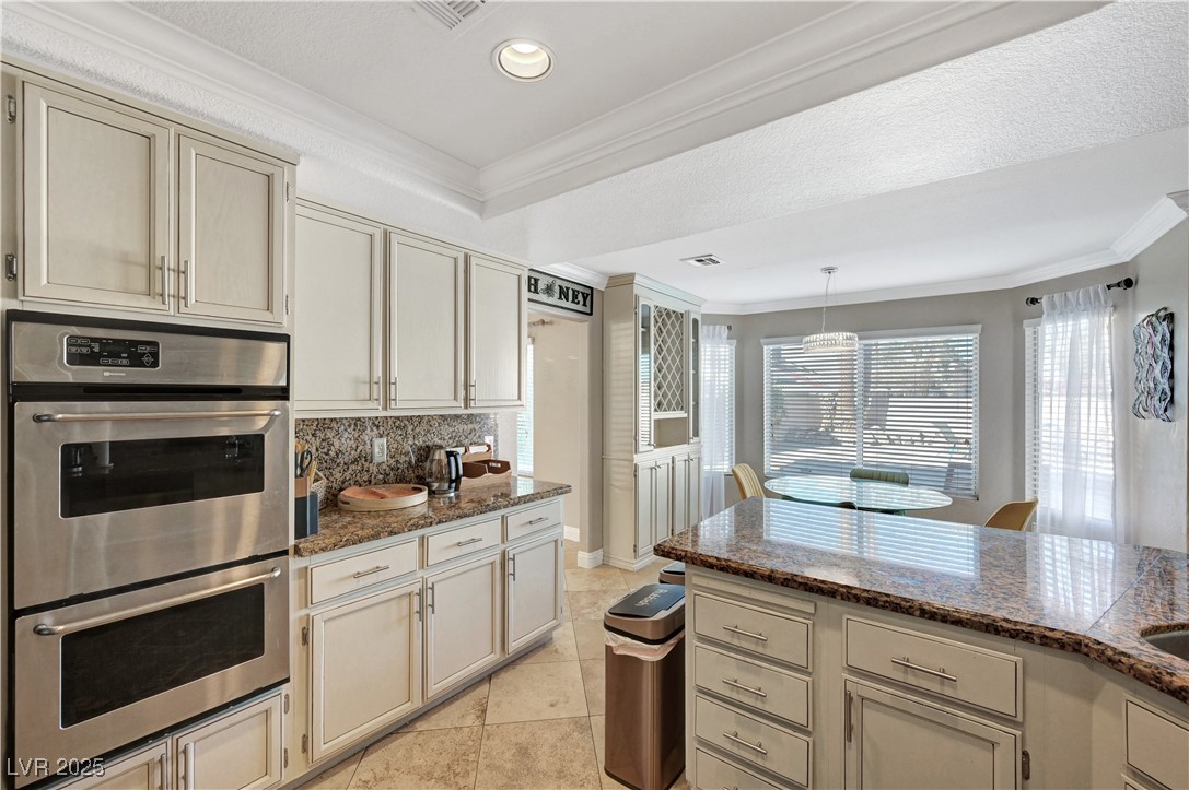 1486 Powder Horn Drive Henderson, NV 89014 - Photo 21 of 99 Kitchen with ornamental molding, double oven, dark stone counters, cream cabinets, and tasteful backsplash