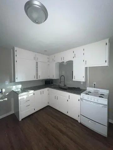 a kitchen with a sink dishwasher and white cabinets with wooden floor