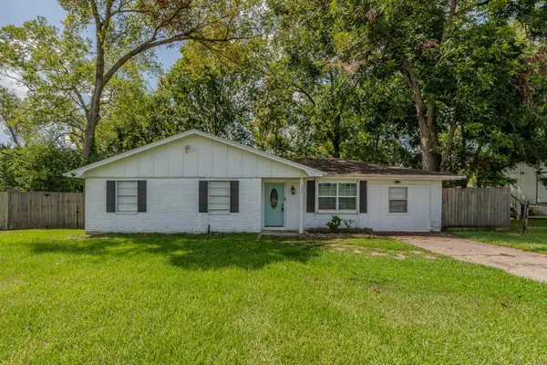 a house that is sitting in the grass with large trees and wooden fence