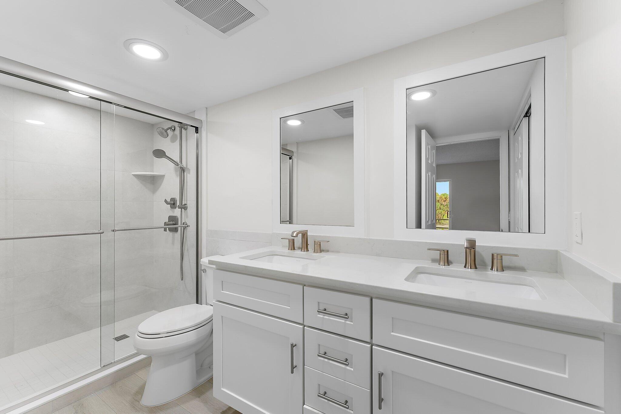 20 Celestial Way, Unit 215 Juno Beach, FL 33408 - Photo 15 of 25 a bathroom with a toilet a sink a glass door a shower a mirror and vanity