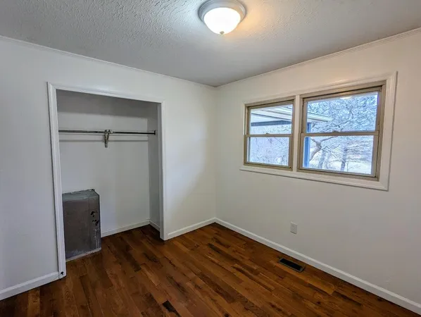 an empty room with wooden floor closet and windows