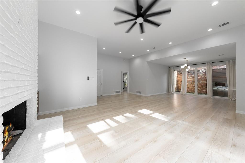 14140 Regency Place Dallas, TX 75254 - Photo 7 of 38 Spacious living area featuring light wood-finish flooring, a painted brick fireplace, a modern ceiling fan, recessed lighting, and a multi-pane glass door opening to an outdoor patio area