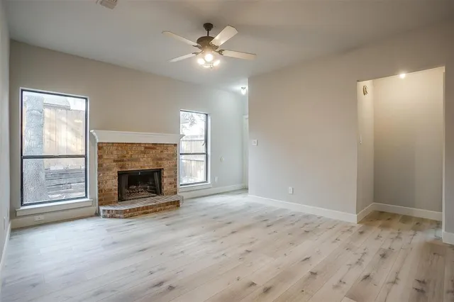 a view of an empty room with wooden floor fireplace and a window