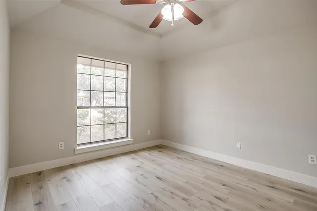 an empty room with wooden floor chandelier fan and windows