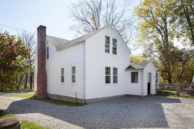 a view of a small white house with a small yard and large tree