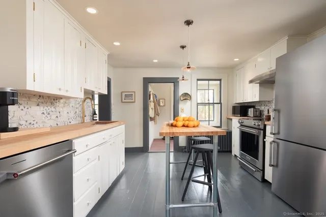 a kitchen with stainless steel appliances a stove a sink a refrigerator white cabinets and wooden floor