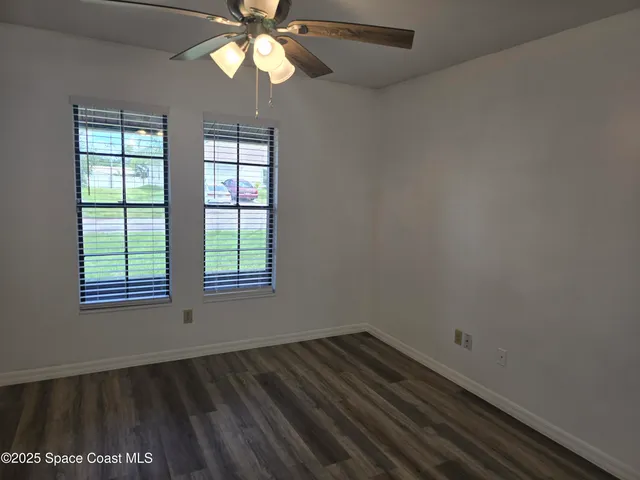 an empty room with wooden floor chandelier fan and windows