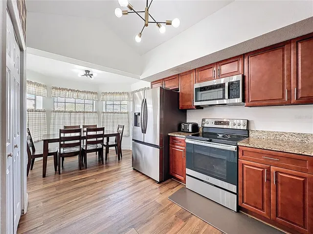 a kitchen with stainless steel appliances granite countertop a stove top oven a refrigerator a dining table and chairs with wooden floor