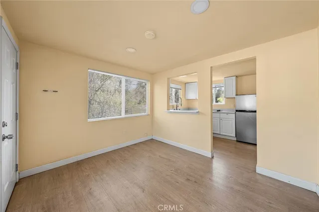 a view of a kitchen and an empty room with a window and wooden floor