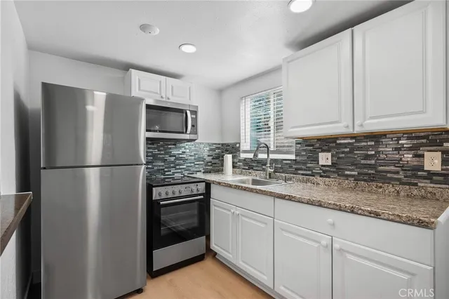a kitchen with stainless steel appliances granite countertop a refrigerator a stove a sink and white cabinets
