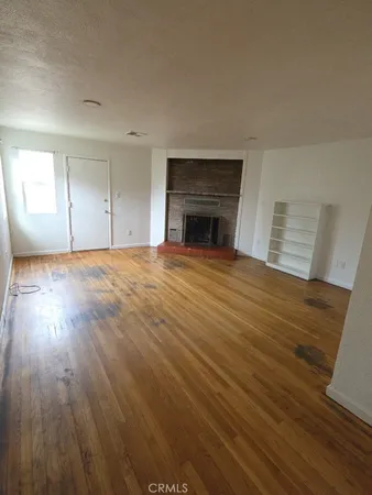 an empty room with wooden floor fireplace and windows