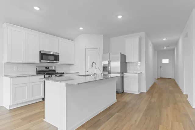 a kitchen with stainless steel appliances a stove top oven a sink a refrigerator white cabinets and wooden floor