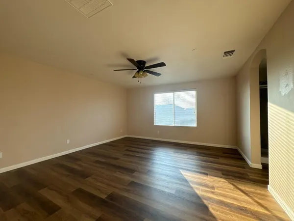 an empty room with wooden floor fan and windows