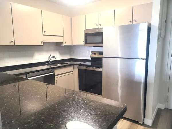 a kitchen with stainless steel appliances granite countertop a refrigerator a stove and a sink with wooden floor