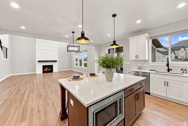 754 West 400 North Mapleton, UT 84664 - Photo 12 of 86 Open-concept living space featuring wood-finish flooring, a contemporary fireplace with a wood mantle, white cabinetry, a large kitchen island with a built-in microwave, and pendant lighting with lots of windows.