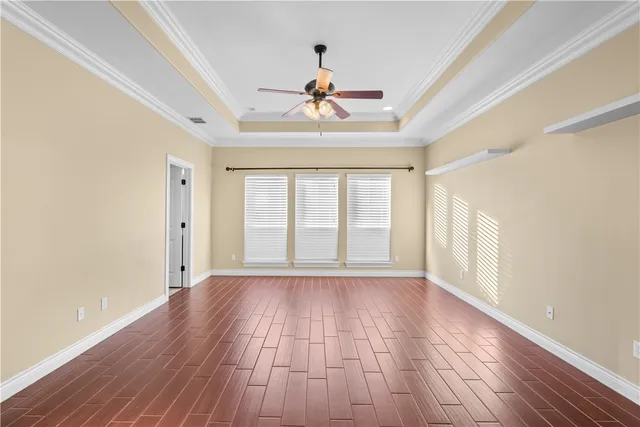 a view of an empty room with wooden floor and a ceiling fan