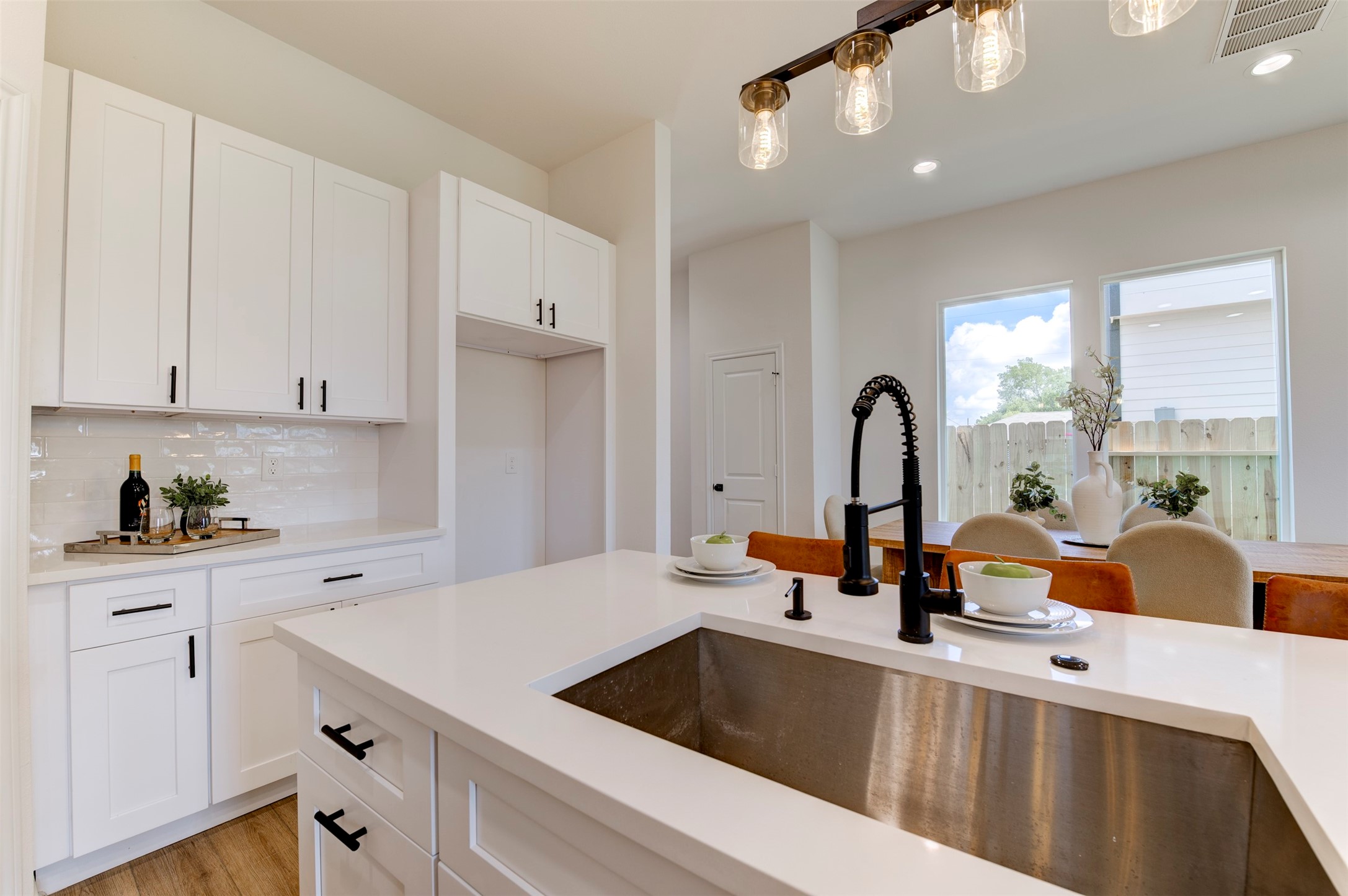 6807 Paris Street Houston, TX 77021 - Photo 20 of 50 Kitchen island with deep stainless farmhouse sink, matte black coil-spring faucet, quartz countertop, white shaker cabinets, subway tile backsplash, and Edison pendant lighting overhead. Back door with yard view visible.