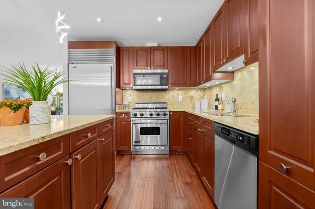 a kitchen with stainless steel appliances granite countertop a refrigerator a sink dishwasher a dining table and chairs with wooden floor