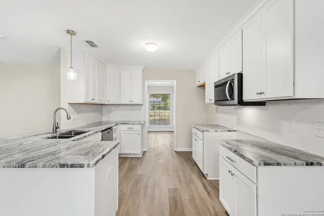 a kitchen with granite countertop a sink a stove top oven and white cabinets