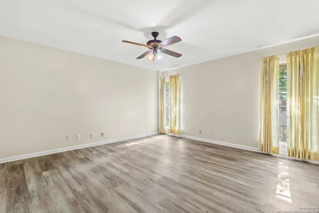an empty room with wooden floor fan and windows