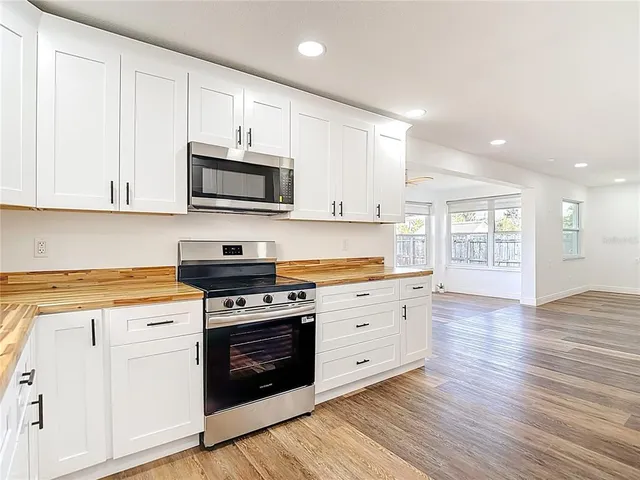 a kitchen with granite countertop a stove top oven a sink dishwasher and white cabinets with wooden floor
