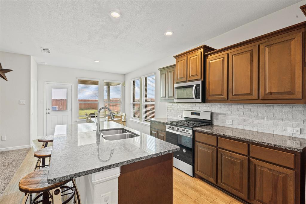 1104 Dublin Drive Cleburne, TX 76033 - Photo 13 of 39 Kitchen featuring dark stone counters, a breakfast bar, appliances with stainless steel finishes, backsplash, and a textured ceiling