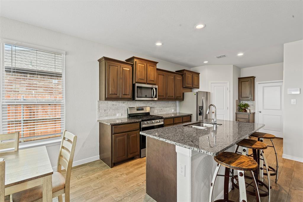1104 Dublin Drive Cleburne, TX 76033 - Photo 14 of 39 Kitchen featuring a breakfast bar area, appliances with stainless steel finishes, tasteful backsplash, dark stone counters, and a kitchen island with sink