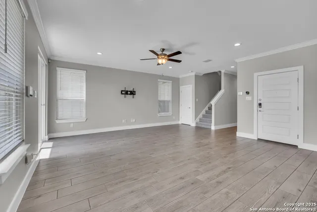 a view of an empty room with wooden floor and a ceiling fan