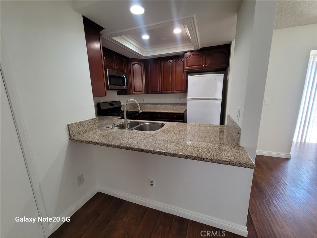 12235 Pine Street, Unit 18 Norwalk, CA 90650 - Photo 2 of 18 a kitchen with granite countertop a sink a refrigerator a microwave and cabinets