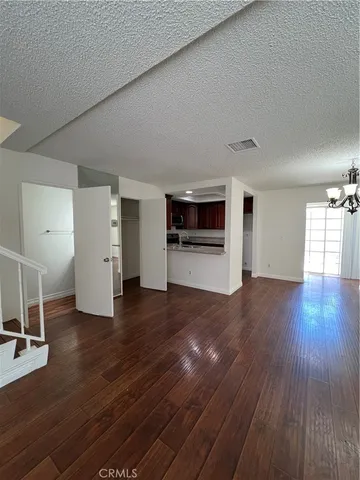 an empty room with wooden floor and kitchen view