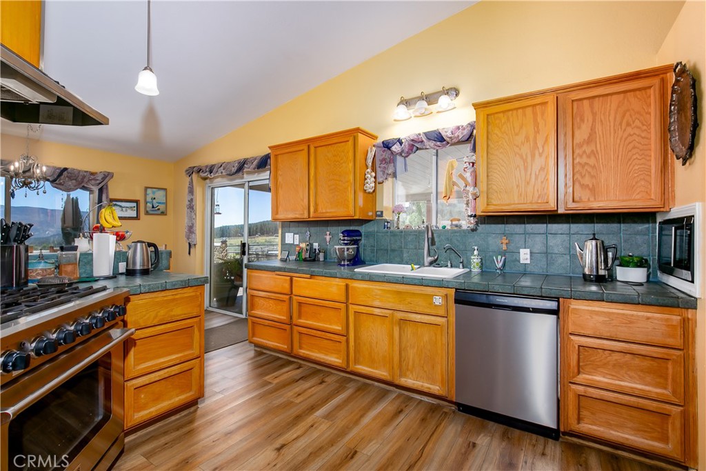 10960 Steinhoff Road Frazier Park, CA 93225 - Photo 26 of 46 A secondary view of the kitchen highlighting the functional workspace. This perspective features an under-mount sink, a stainless steel dishwasher, a classic teal-tiled backsplash, and abundant warm wood cabinet storage, all adjacent to sliding glass doors that open to the outdoor deck area.