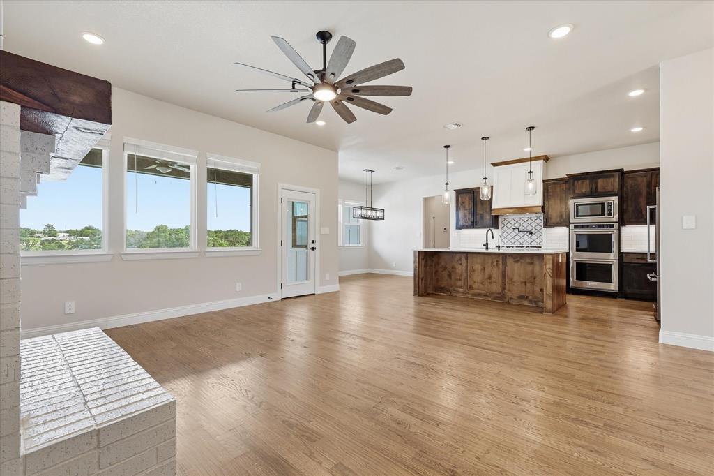 120 Grace Vw Road Weatherford, TX 76088 - Photo 11 of 40 Open-concept living space featuring wood-finish flooring, a modern kitchen island with pendant lighting, a white brick fireplace, recessed lighting, and large windows with outdoor scenery