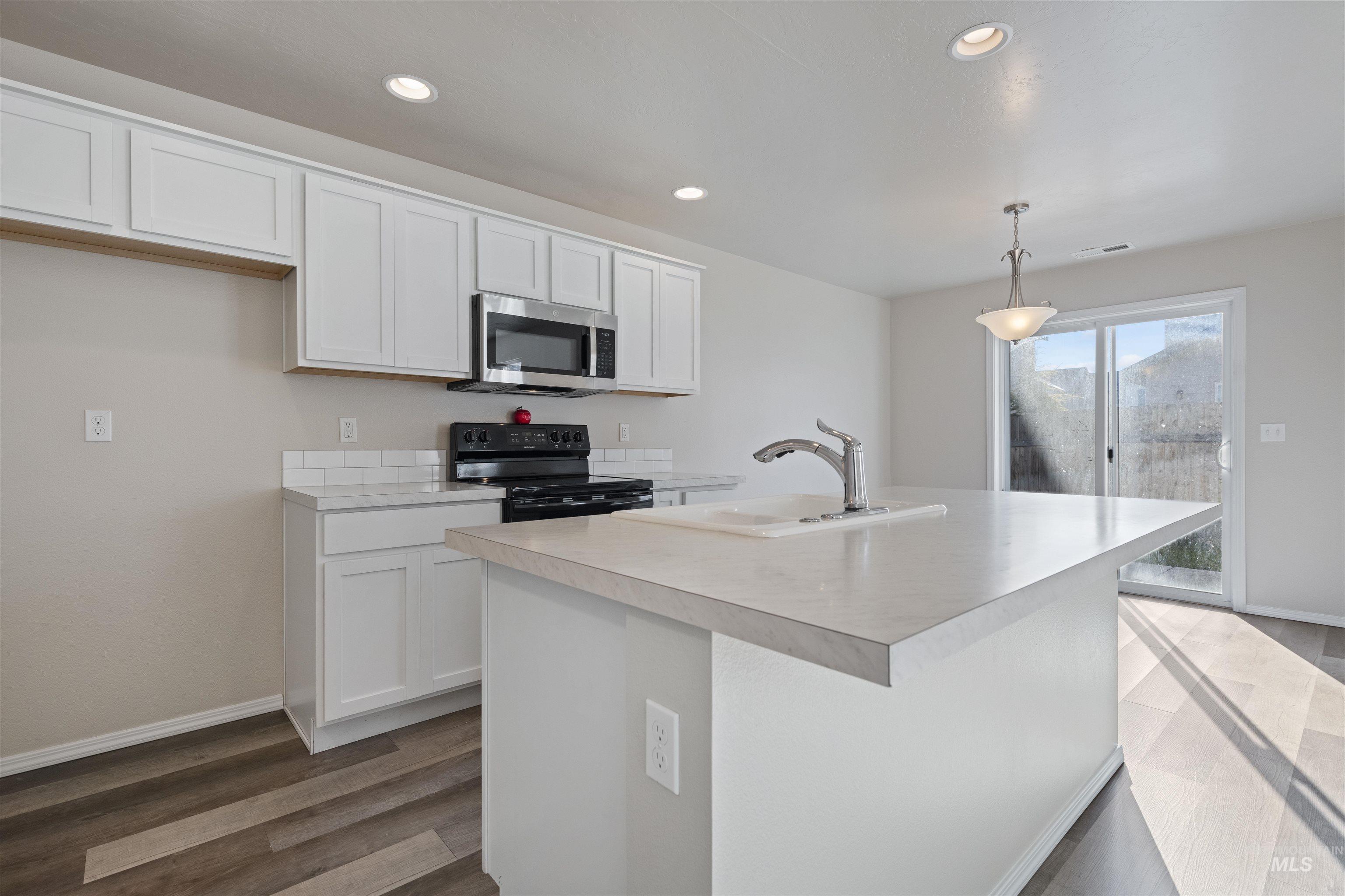 13559 Cocoa Beach Way Caldwell, ID 83607 - Photo 11 of 28 Kitchen with black electric range oven, white cabinetry, light countertops, stainless steel microwave, and hanging light fixtures