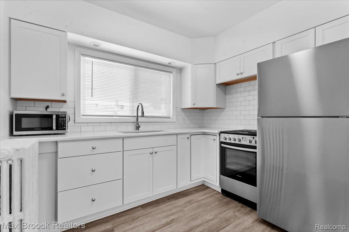 513 West 9 Mile Road, Unit 1 Hazel Park, MI 48030 - Photo 10 of 21 White cabinetry with brushed nickel hardware, stainless steel appliances, white subway tile backsplash, white countertops, and wood-finish flooring