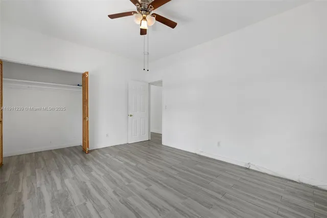 an empty room with wooden floor fan and windows